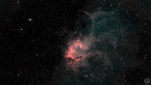 Fotografia astronómica de campo amplo evidenciando a Nebulosa do Leão (SH2-132). Destaca-se uma estrutura central brilhante e densa de tons vermelho rubro e rosa flamejante, que transita suavemente para uma expansa e difusa coroa de gás azul anil no quadrante superior direito. O rico fundo negro do espaço encontra-se texturado por subtis poeiras escuras e intensamente pontilhado por milhares de estrelas nítidas.
