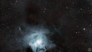 Fotografia astronómica profunda exibindo a Nebulosa da Íris (NGC 7023) no centro, caracterizada por um núcleo estelar brilhante intensamente rodeado por delicadas e complexas nuvens de poeira reflectora de tons azuis e anil. Todo o campo em torno da nebulosa revela extensas e imponentes massas de poeira escura e acastanhada que bloqueiam a luz de fundo. A imagem encontra-se ponteada por estrelas nítidas de diversas colorações sobre um céu negro e profundo.